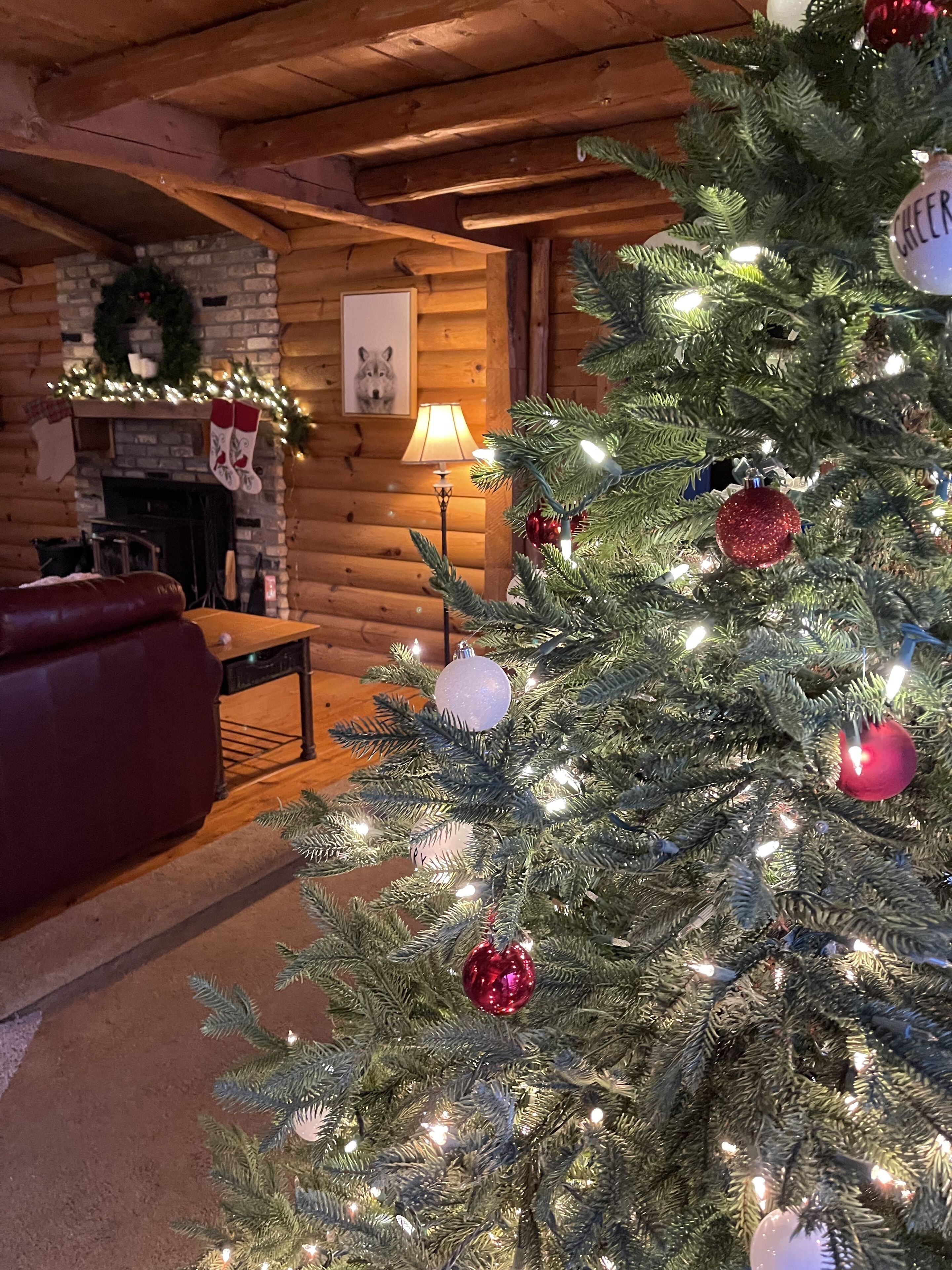 Un interior acogedor de cabaña de madera con un árbol de Navidad decorado, una chimenea y un sofá de cuero rojo.
