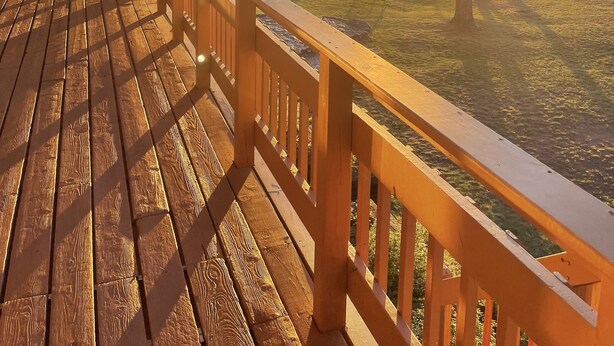 A wooden deck with a railing overlooking a lake, surrounded by trees and a dock with a boat.