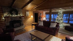 A cozy log cabin interior with a fireplace, leather furniture, a Christmas tree, and a stone wall.