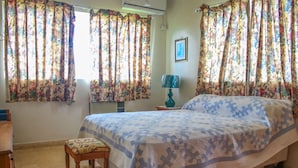 A bedroom with a bed, a chair, a lamp, and curtains. - Rica Vista Beach Cottages (Boscobel)