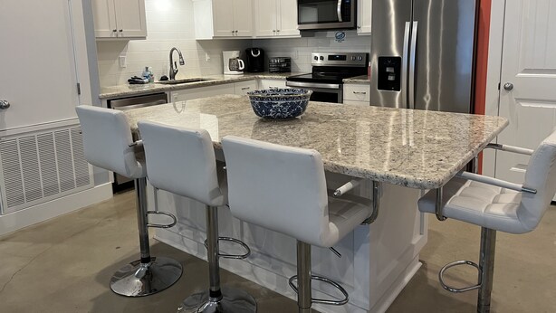 A modern kitchen with white cabinets, a granite countertop, a stainless steel refrigerator, and a coffee maker. - Perfect for fishermen and families for your stay in Port O'Connor! (Port O'Connor)