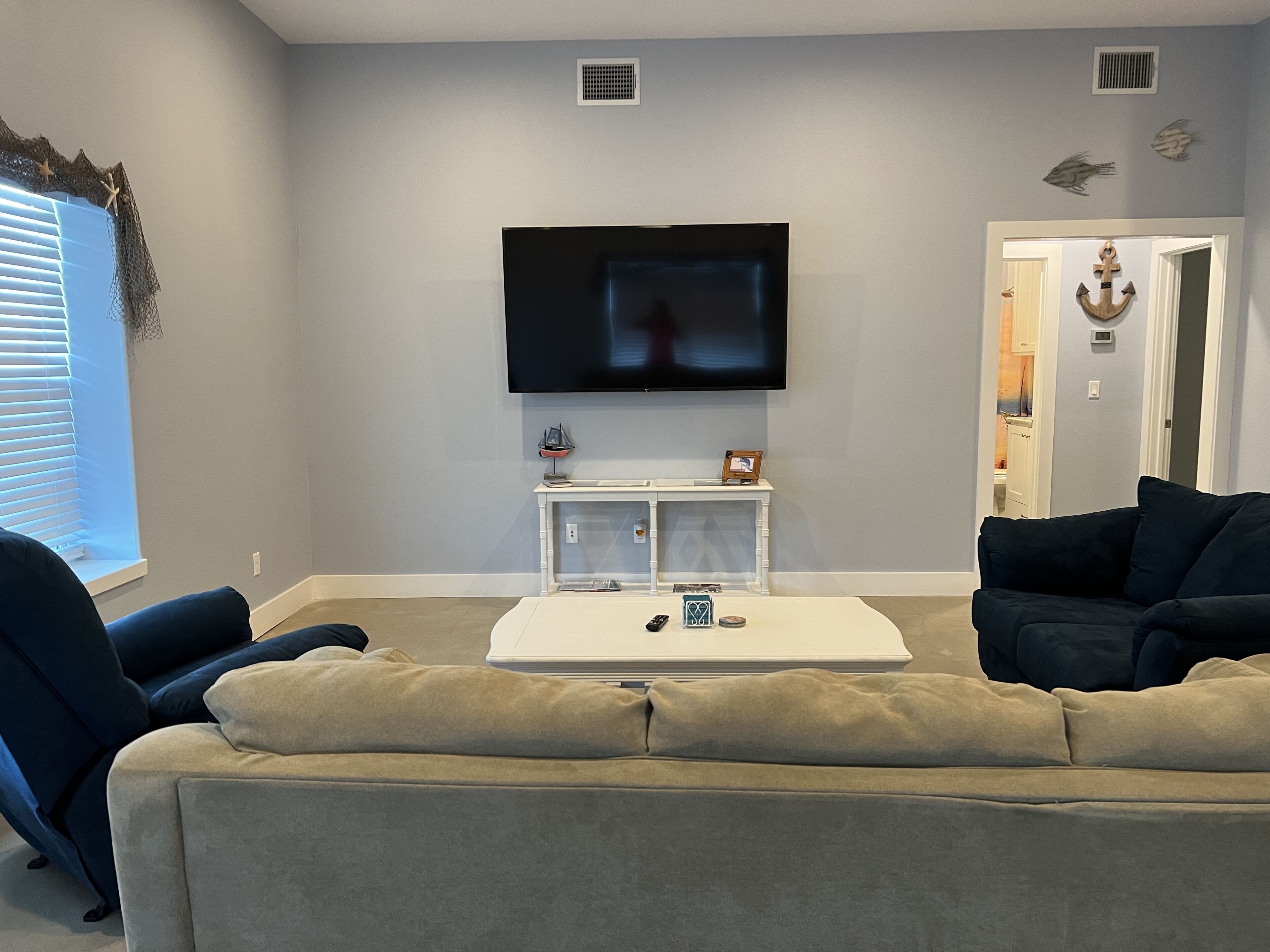 A living room with a flat-screen TV mounted on the wall, a white console table with decorative items, a beige sofa, and a dark-colored couch.