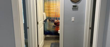 A hallway with a door leading to a bathroom featuring a maritime-themed shower curtain.
