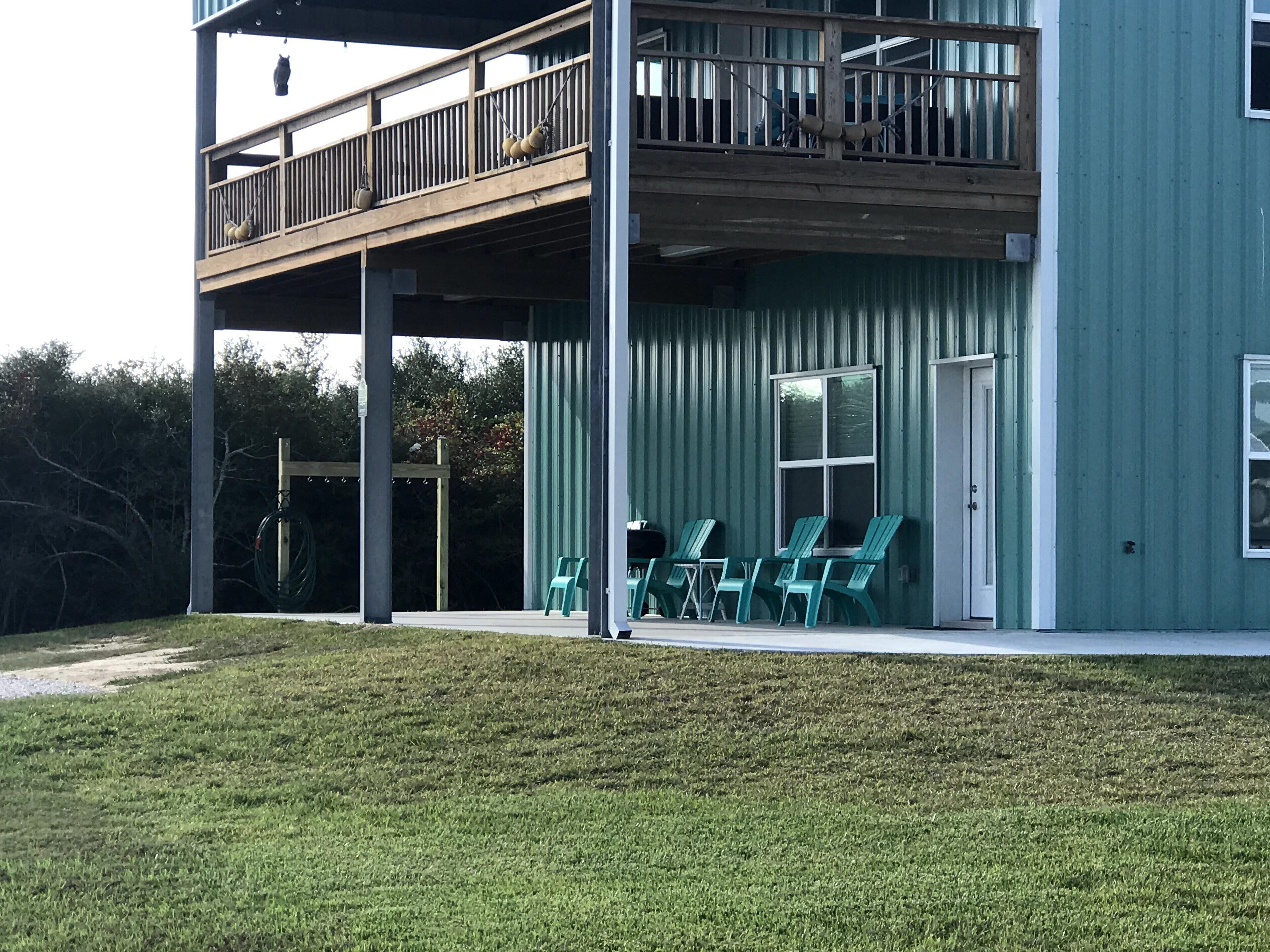 A two-story building with a balcony, outdoor seating area with chairs, and a grassy lawn.