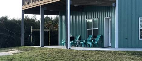 A two-story building with a balcony, outdoor seating area with chairs, and a grassy lawn.