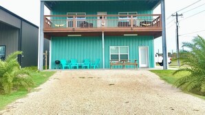 A two-story building with a balcony on the upper floor, a gravel driveway, and outdoor seating. - Perfect for fishermen and families for your stay in Port O'Connor! (Port O'Connor)