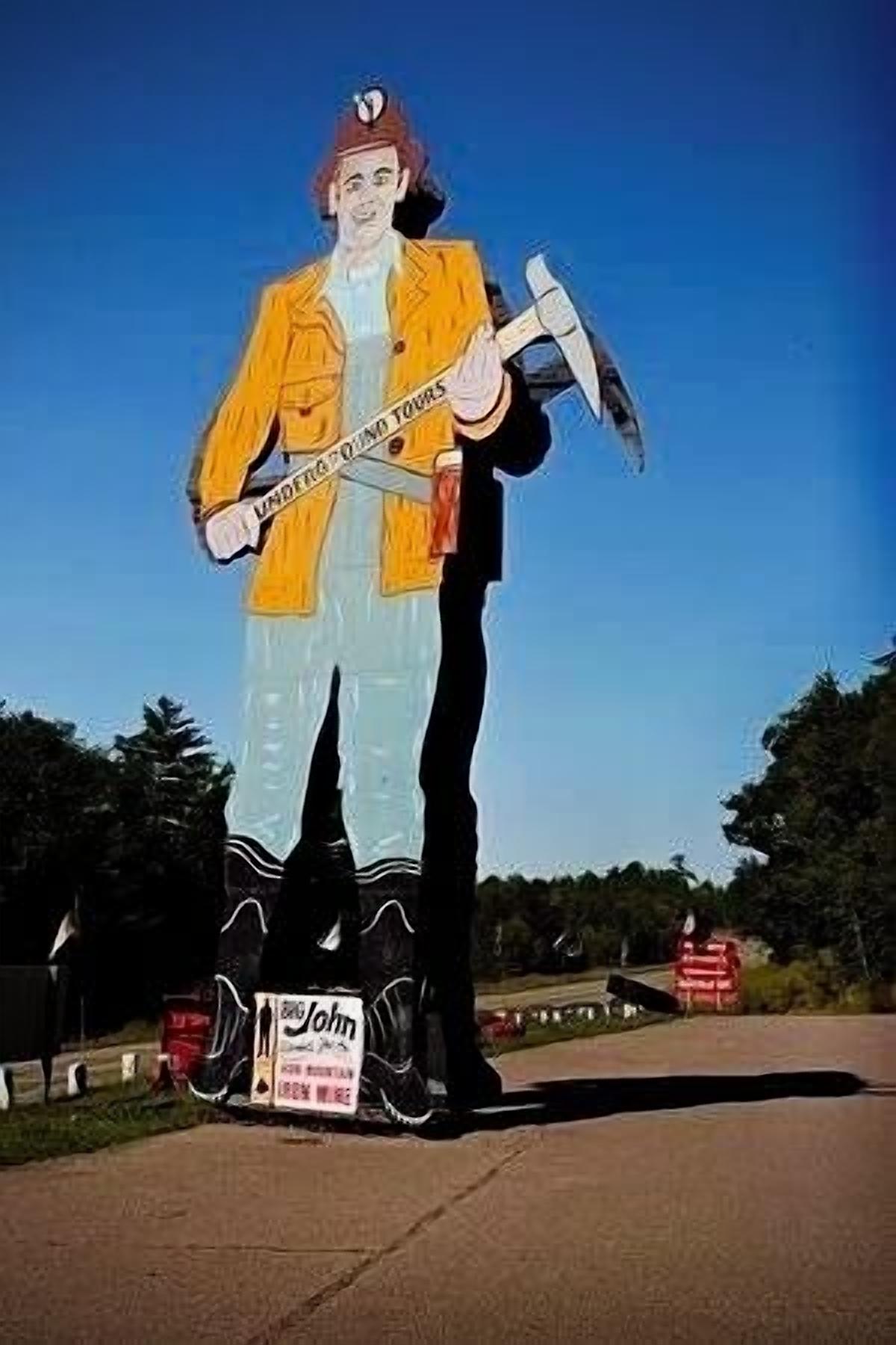 A large outdoor sculpture of a man holding a hammer and a sign that reads "John".
