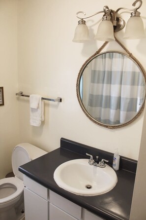 A bathroom with a white sink, a round mirror with a rope frame, and a toilet. - Beautiful Cottage on Spread Eagle Chain of Lakes (Florence)