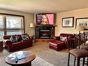 Una sala de estar con chimenea, muebles de cuero y un televisor montado en la pared.