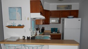 Una cocina con armarios de madera, un refrigerador blanco, un microondas, un lavaplatos y dos taburetes de bar.