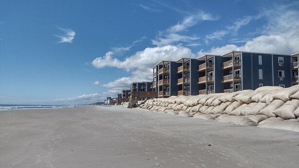 Un hotel frente a la playa con varios balcones, una playa de arena y un cielo despejado.