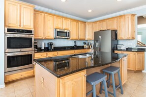 A modern kitchen with wooden cabinets, stainless steel appliances, a granite countertop, and two bar stools. - Sunset Island 18 Beach Walk Lane (Ocean City)