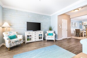 A living room with a flat-screen TV, two patterned armchairs, a white cabinet, and a blue rug.