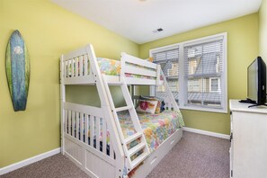 Un lit superposé avec une échelle, une décoration sur le thème du surf, une fenêtre avec des stores et un téléviseur posé sur un meuble.