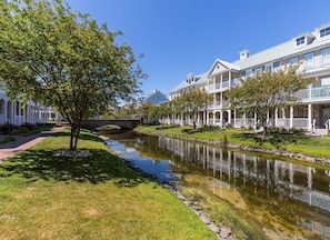 A residential area with a narrow water channel, white houses with balconies, and a tree-lined pathway.