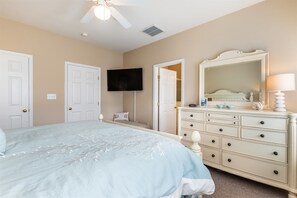 Un dormitorio con cama, cómoda, televisor y una puerta que da a otra habitación.