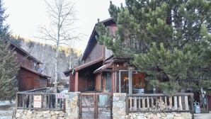 Una cabaña rústica con cimientos de piedra y fachada de madera, que cuenta con un porche y una chimenea visible.