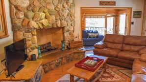 Una chimenea de piedra, un televisor, un sofá de cuero y un cartel que dice 'Welcome to the Mountains'.