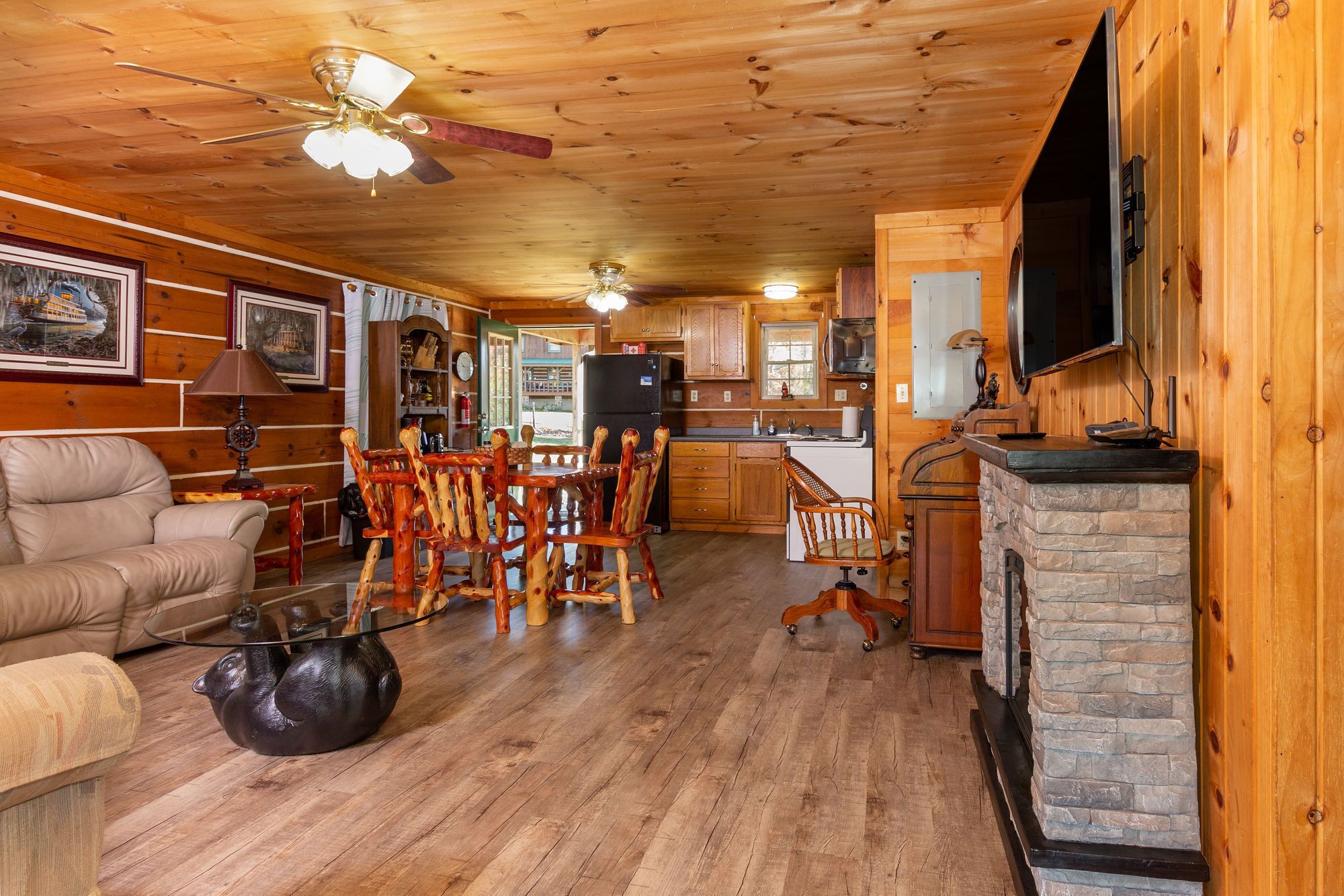 Un intérieur de chalet chaleureux avec un plafond en bois, une cheminée en pierre, un coin repas avec des chaises en bois, une cuisine avec des meubles en bois et un canapé en cuir.