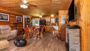 A cozy cabin interior with a wooden ceiling, a stone fireplace, a dining area with wooden chairs, a kitchen with wooden cabinets, and a leather sofa. - Valentine Drive Cabin 2 (Lookout Mountain)
