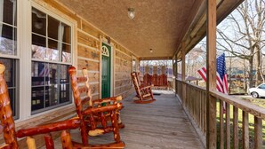 A wooden porch with rocking chairs and American flags, leading to a green door. - Valentine Drive Cabin 2 (Lookout Mountain)