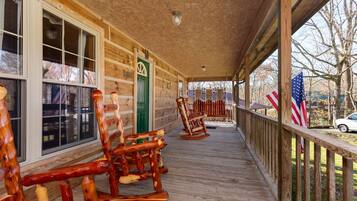 A wooden porch with rocking chairs and American flags, leading to a green door.
