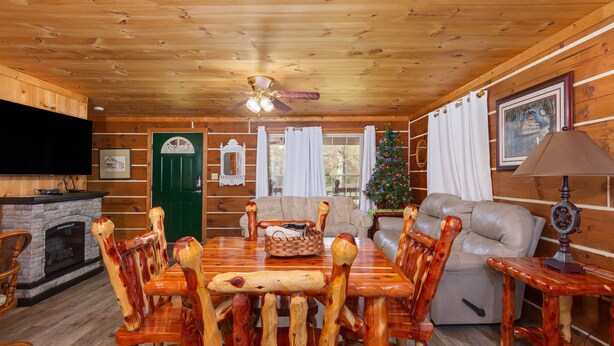 A wooden cabin interior with a dining table surrounded by wooden chairs, a fireplace, a sofa, and a Christmas tree. - Valentine Drive Cabin 2 (Lookout Mountain)