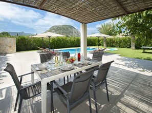 Un espacio de comedor al aire libre con una mesa dispuesta para cuatro, con vista a una piscina y un paisaje montañoso.