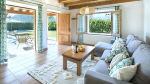 A living room with a sofa, a wooden coffee table, and a view of a garden through large windows. - VILLA  DIVINA - LUXURY RETREAT (Pollensa)