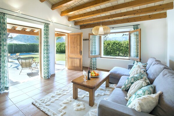 A living room with a sofa, a wooden coffee table, and a view of a garden through large windows. - VILLA DIVINA - LUXURY RETREAT (Pollensa)