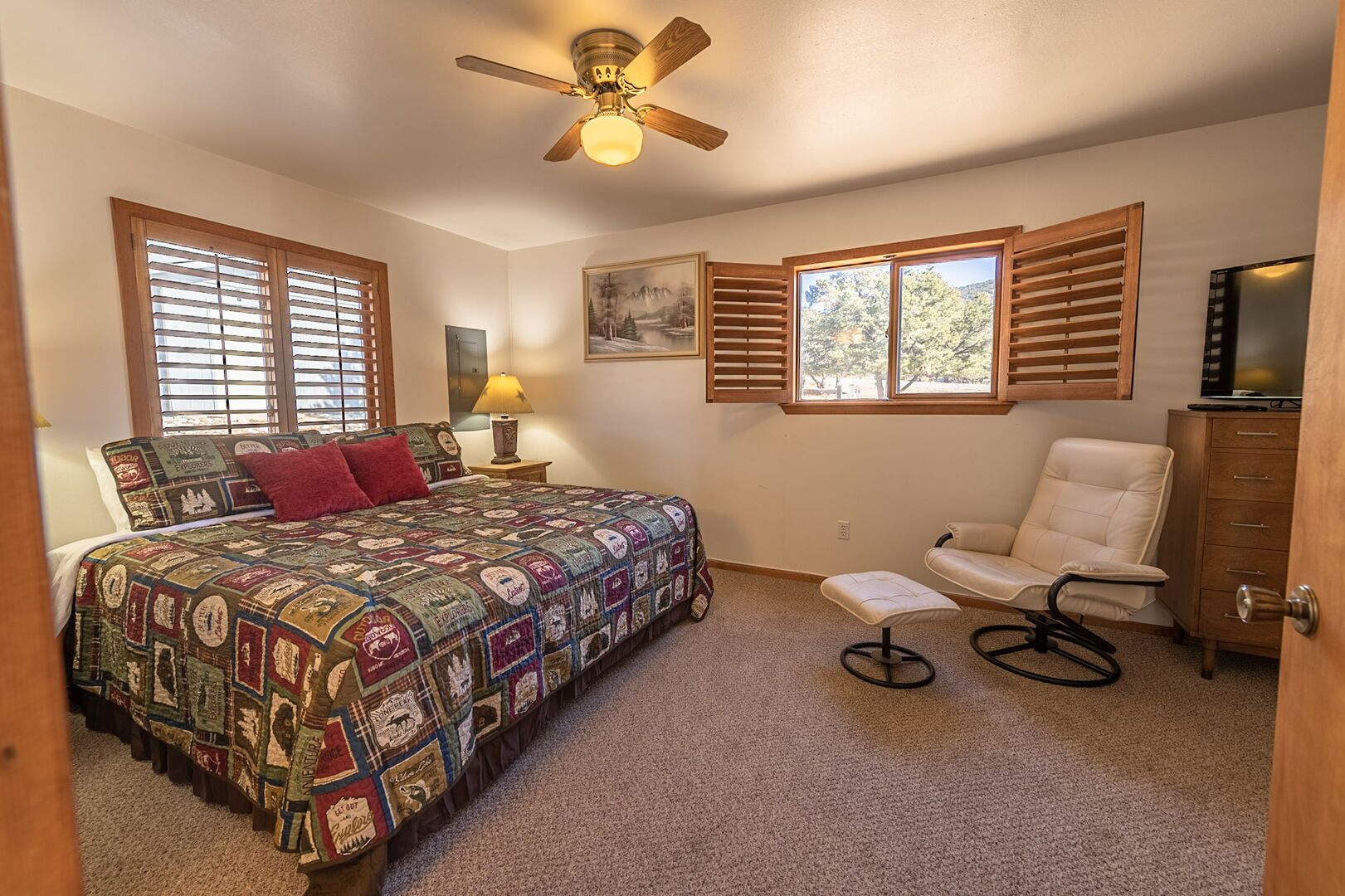 Une chambre à coucher comprenant un lit, une chaise, un bureau, un ventilateur de plafond et une fenêtre avec des stores.