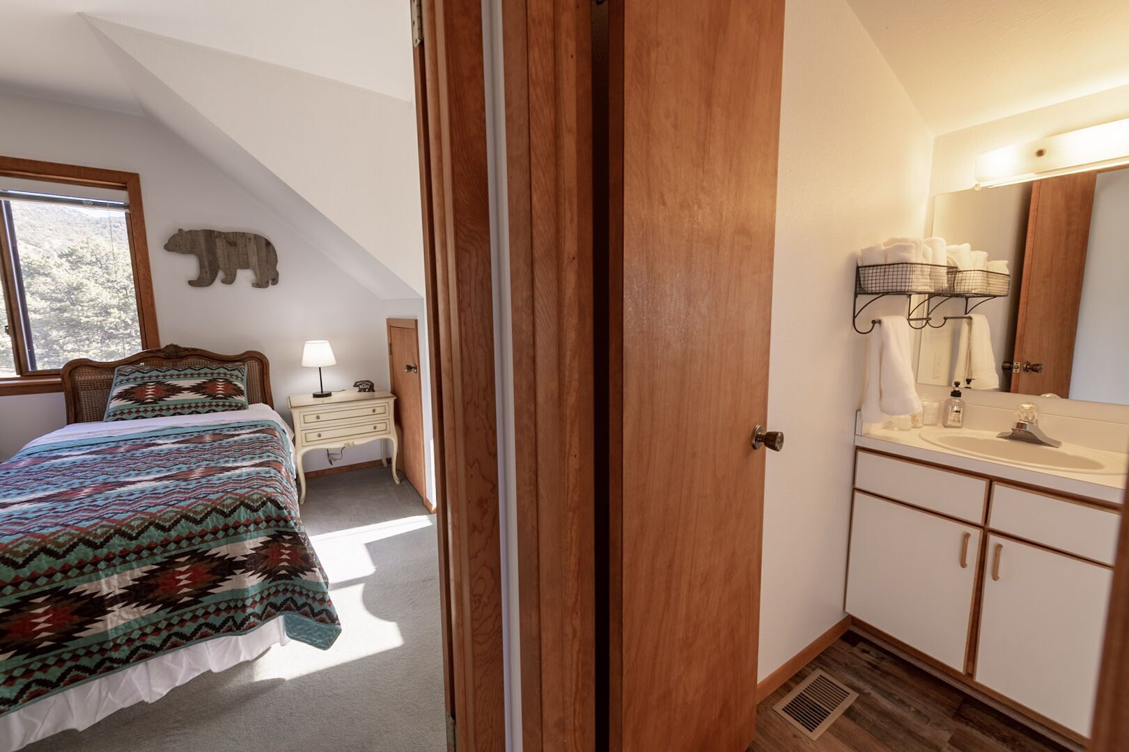 Une chambre à coucher comprenant un lit, une table de chevet avec une lampe, une commode et une salle de bain avec un lavabo et un miroir.