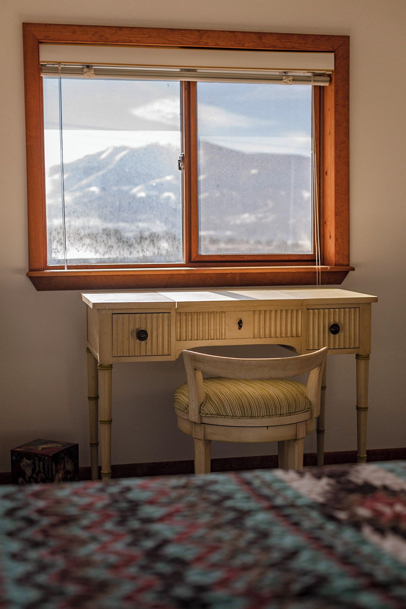 A wooden desk with a chair, a window with a view of mountains, and a patterned rug.