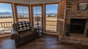A cozy living room with a leather sofa, a fireplace, and a view of mountains through large windows. - Rhode's Hideaway- Dog Friendly, Minutes to Salida, Close to Monarch (Salida)