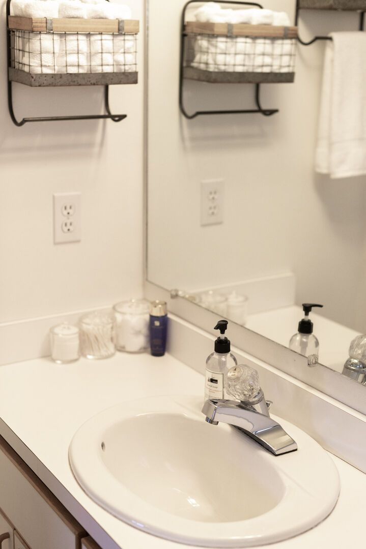 A bathroom with a white sink, a mirror, and two towel racks with folded towels.