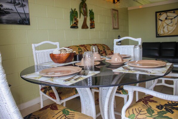 A dining area with a glass-top table, white wicker chairs, and a floral cushion.