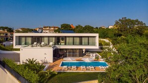 Een modern huis met twee verdiepingen, een ruim glazen balkon, een zwembad en een verzorgde tuin.