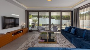 Een moderne woonkamer met een flatscreen televisie, een blauwe bank, een glazen salontafel en een houten tv-meubel.