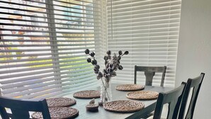 A dining table with woven placemats, a vase with dried flowers, and dark wooden chairs. - Yard, Dog, & Kid Friendly! -Blue Whale Inn #C (San Clemente)
