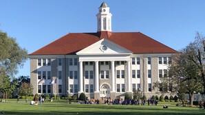 A large building with a central tower, a clock, and a lawn in front.