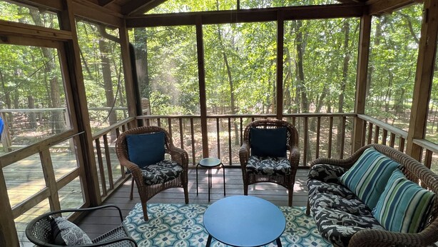 A covered outdoor seating area with wicker furniture, a patterned floor, and a view of a forest.