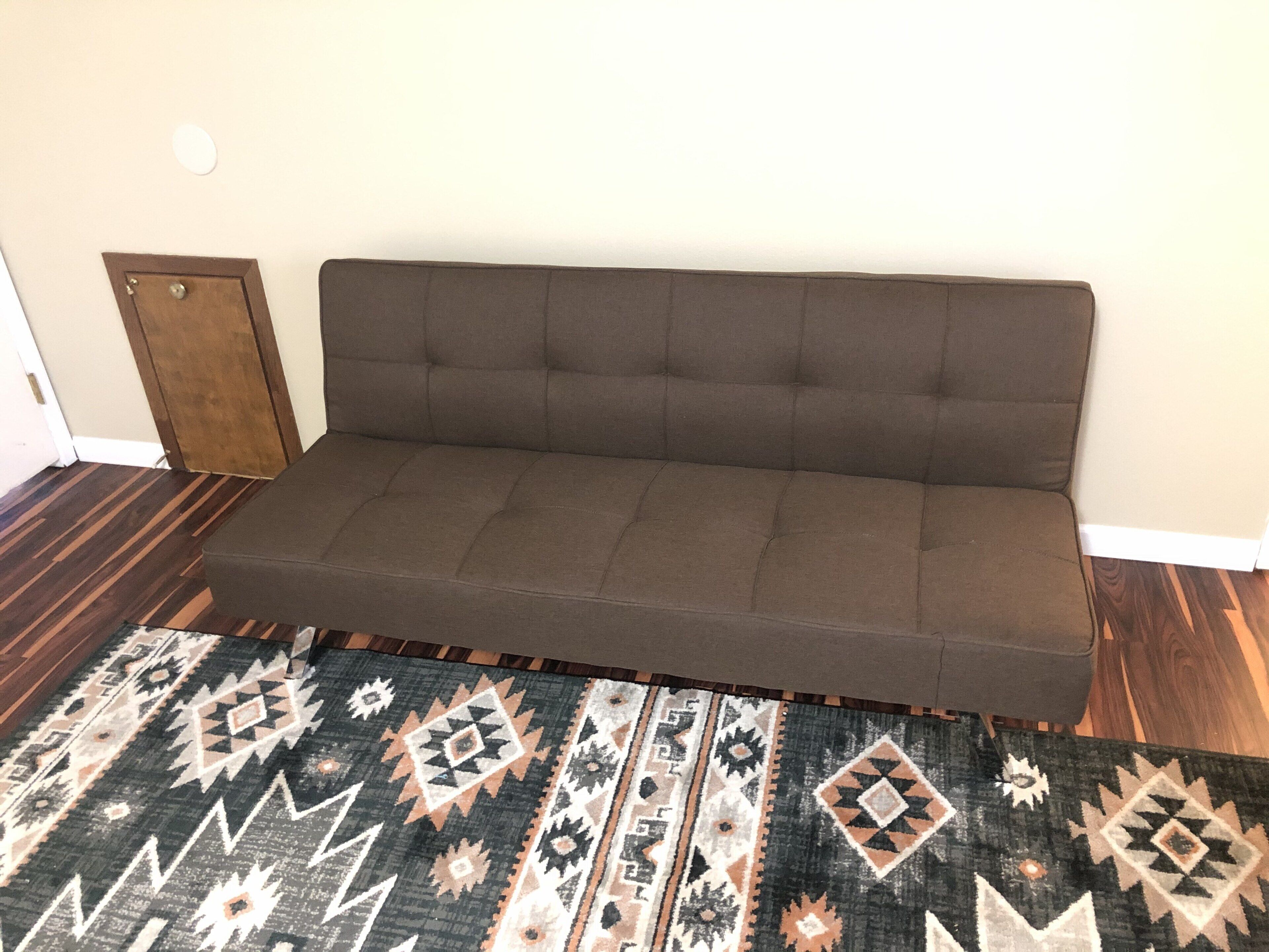 Un canapé marron, avec un tapis à motifs devant.