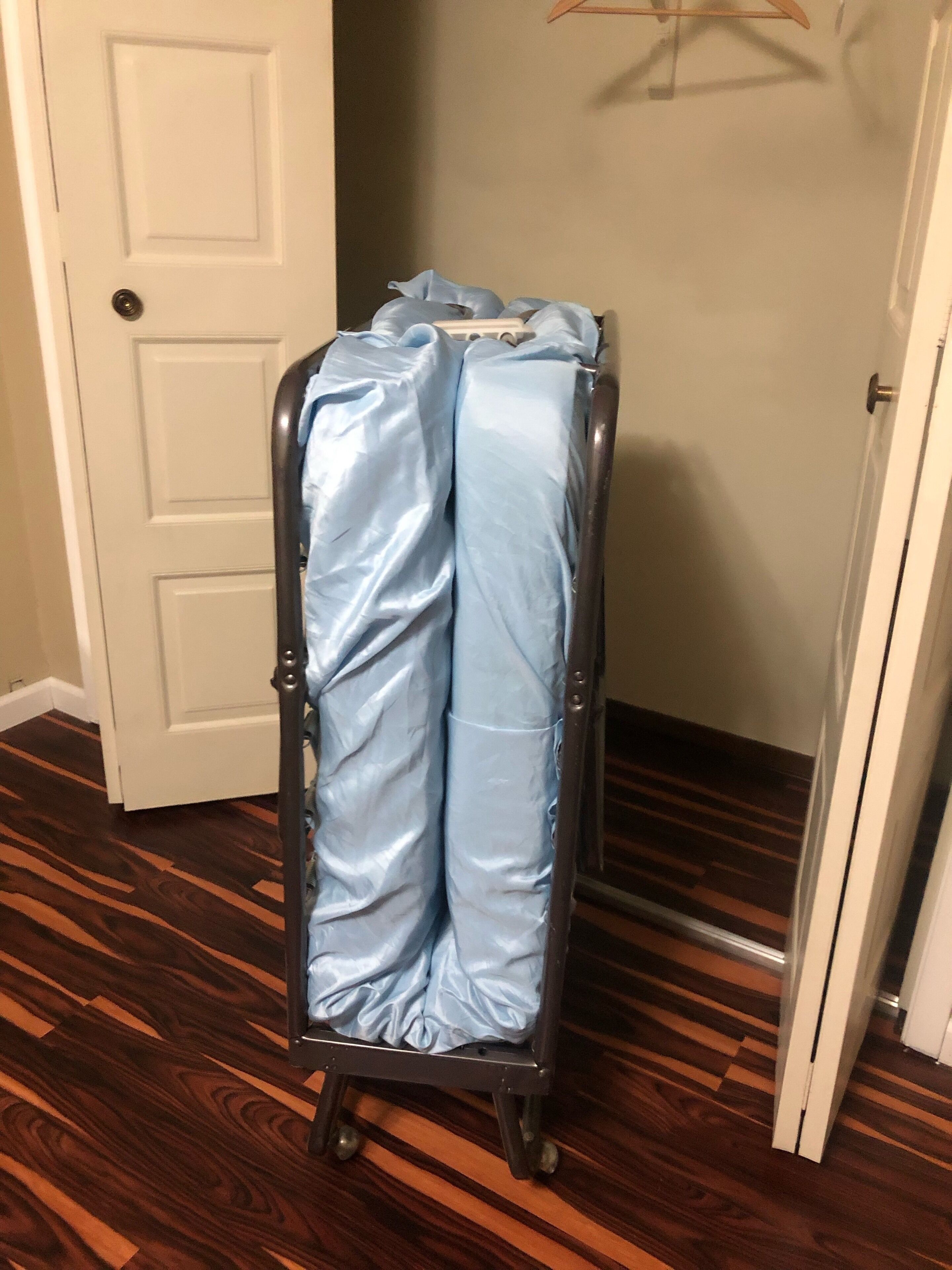 A metal cart with a blue cover, positioned in a hallway with wooden flooring and a white door in the background.