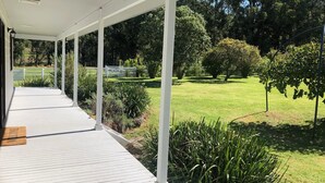 A covered outdoor area with a wooden deck, surrounded by greenery and trees.