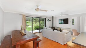 A spacious living area with a wooden table, a sofa, and a TV mounted on the wall.