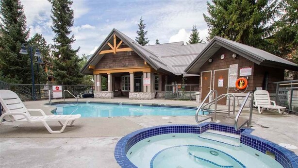 A pool area with lounge chairs, a hot tub, and a wooden building with a metal roof.