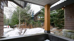 A covered outdoor area with a wooden column, snow on the ground, and a building in the background.