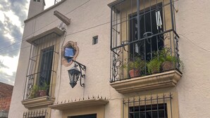 Un edificio con varias ventanas, algunas con rejas, y un balcón con macetas.