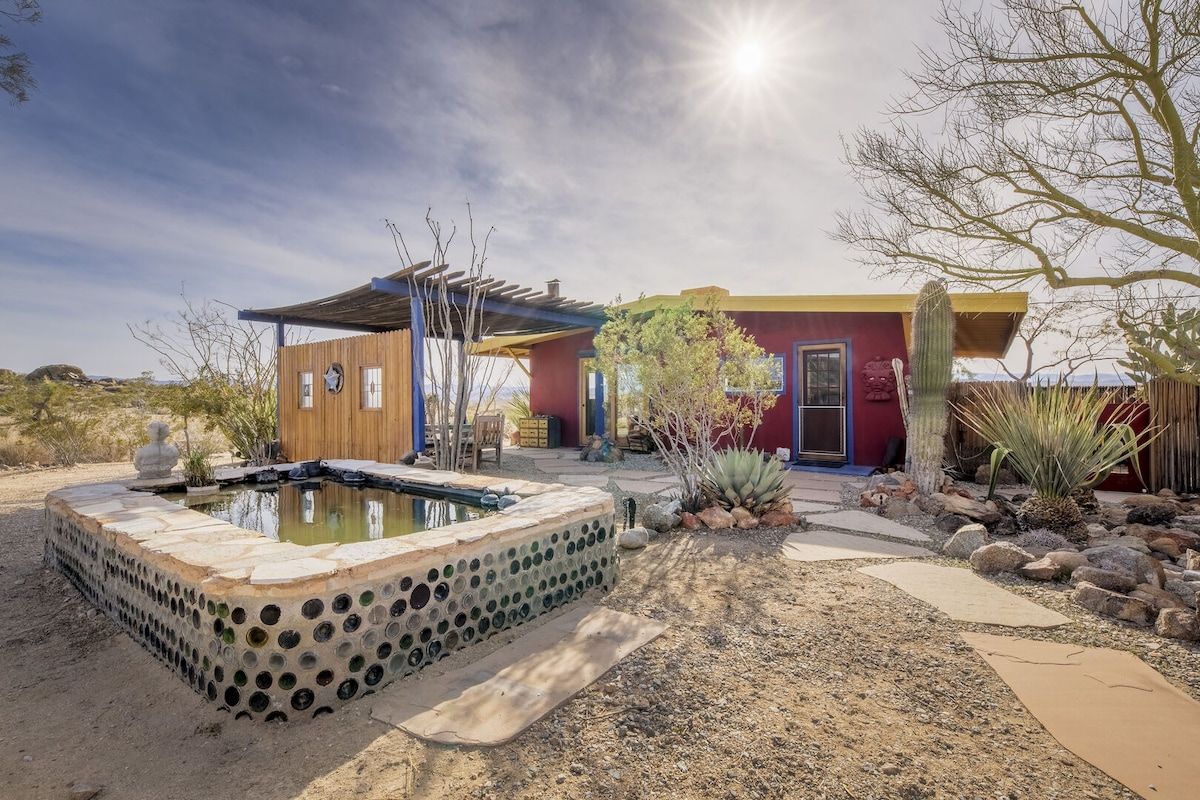 A desert-style building with a pool, surrounded by cacti and a clear sky.