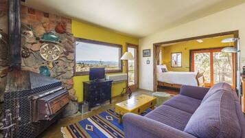 A room with a stone fireplace, a bed, a sofa, and a view of the outdoors.
